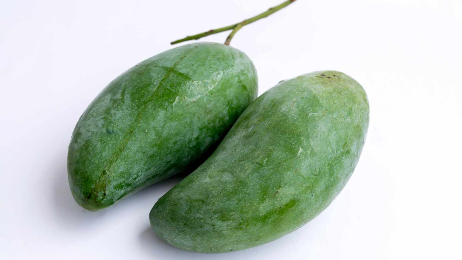 Two whole unripe green mangoes with stems, placed on a white background.