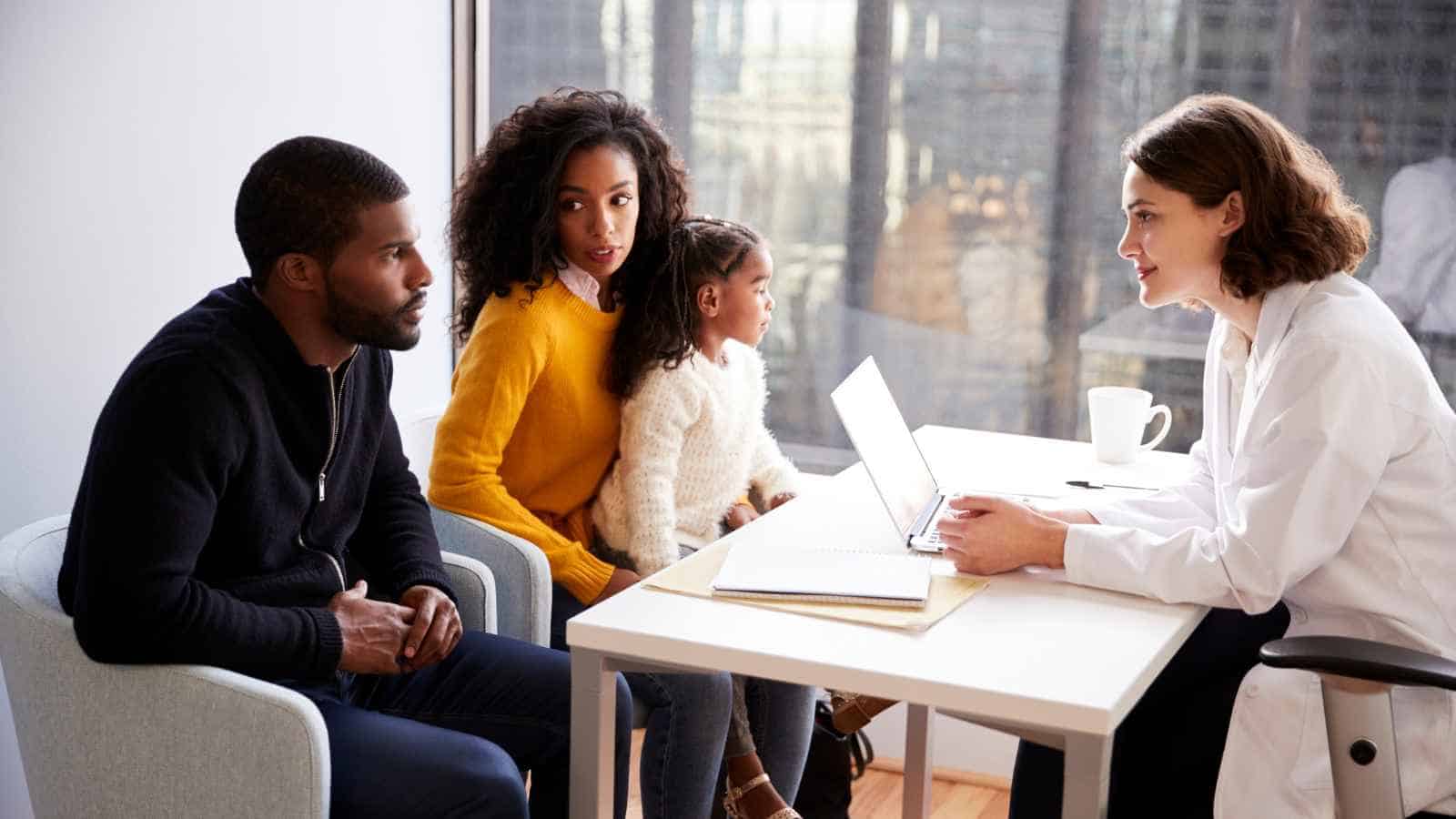 A family sits across from a female doctor at a desk, discussing something together in a medical office setting.