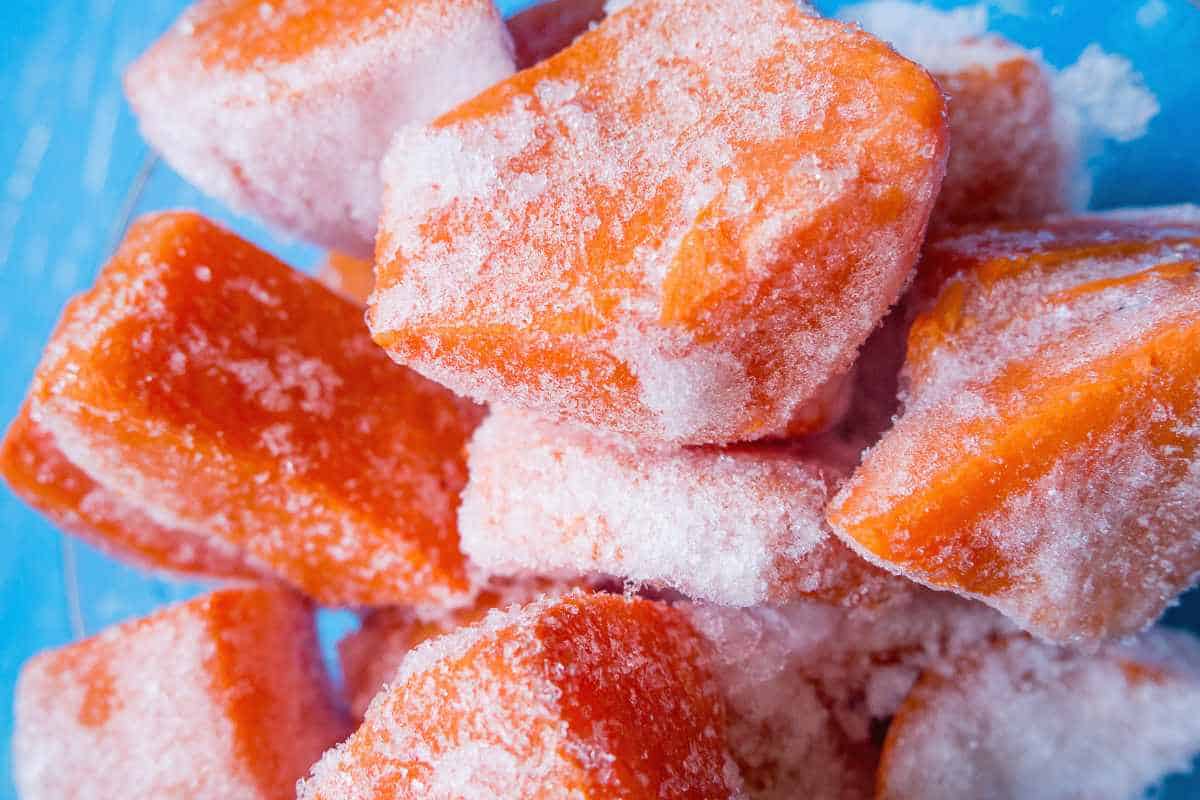 Close-up of several pumpkin chunks covered in frost, stacked loosely against a blue background.