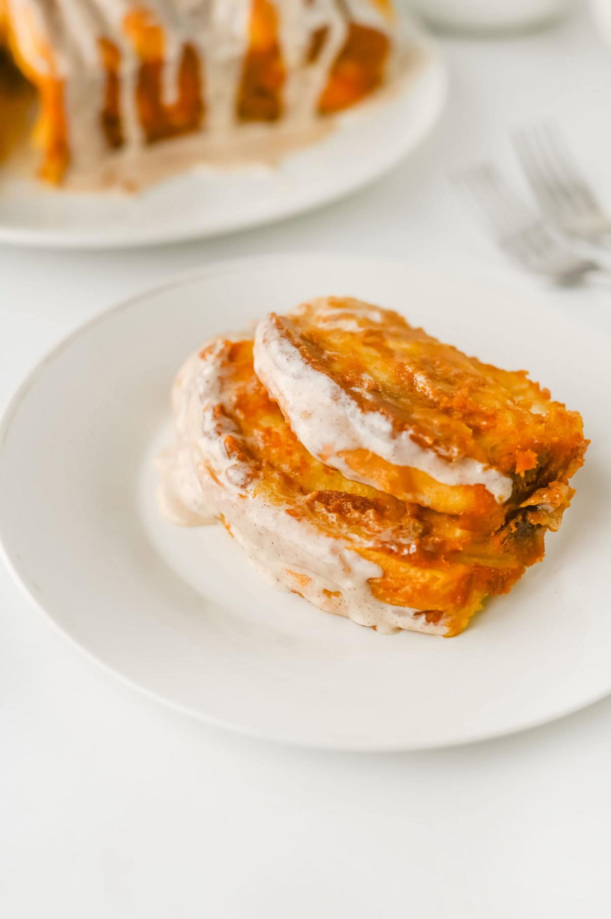 Two slices of glazed pull-apart bread are served on a white plate, with more bread and two forks visible in the background.