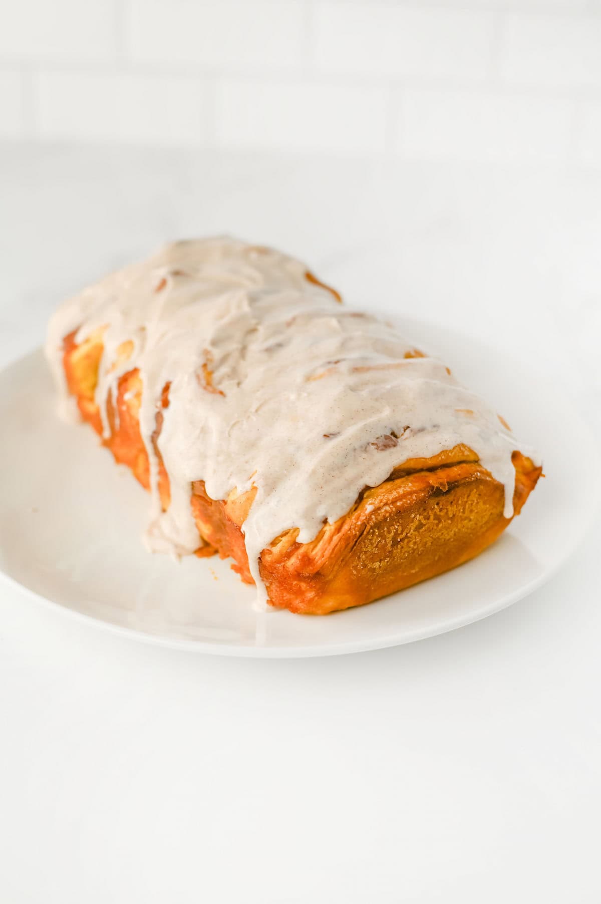 A pumpkin spice pull apart bread with white icing drizzled on top, displayed on a white plate against a plain background.