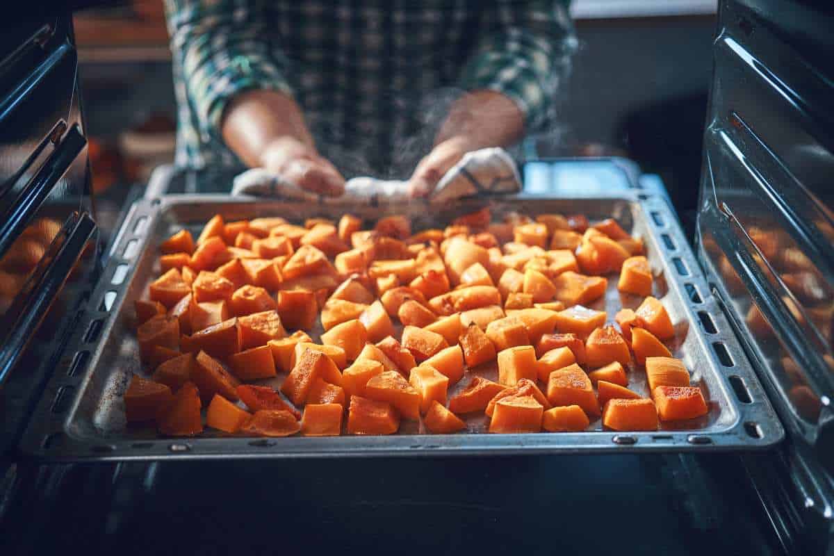 A person removes a baking tray filled with roasted pumpkin cubes from the oven.