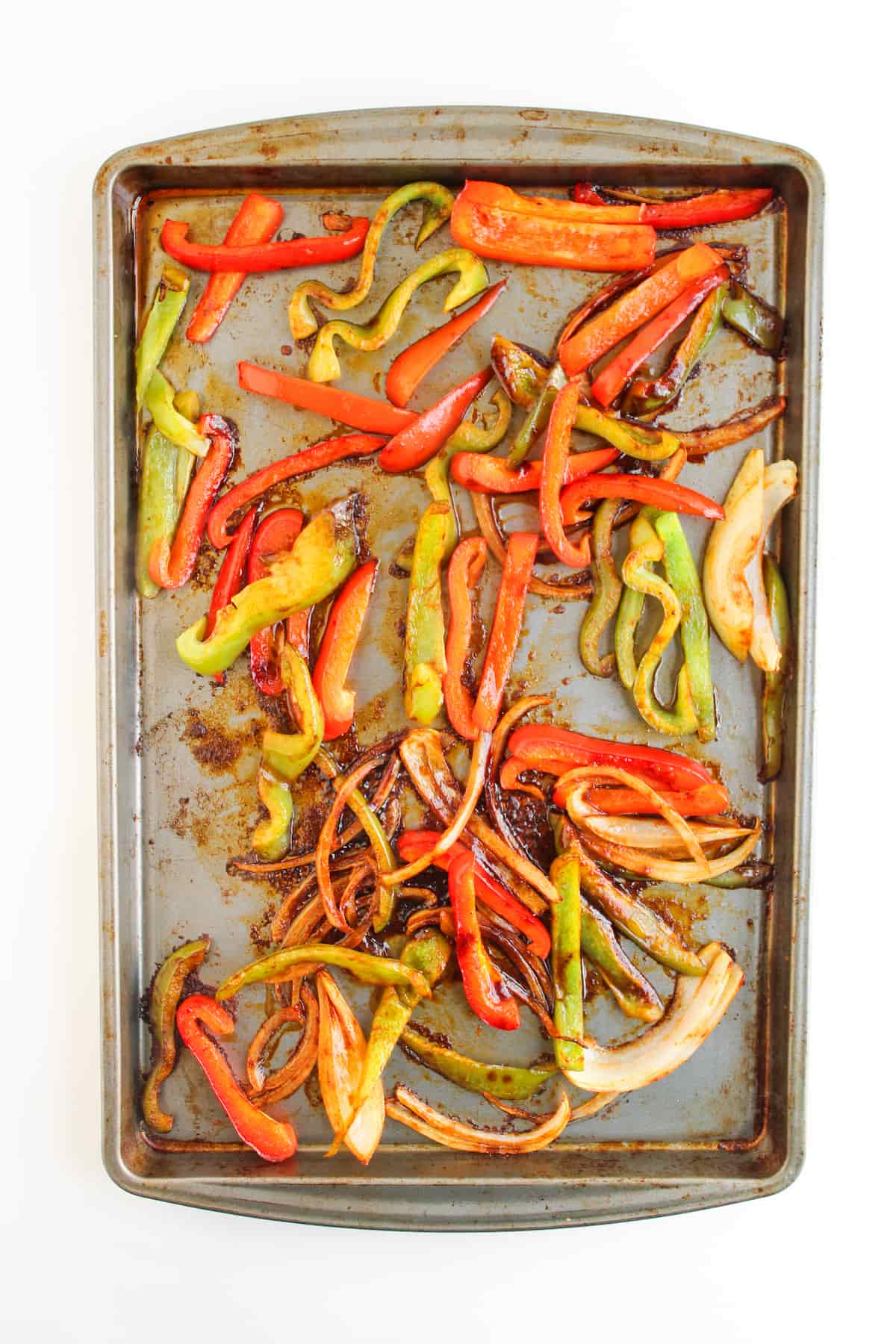 Sliced red and green bell peppers and onions roasted on a metal baking sheet.