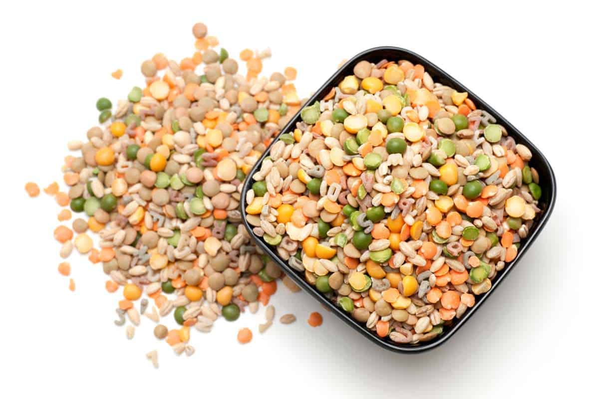 A black bowl filled with a mix of dried lentils and split peas, with some spilled onto a white surface.
