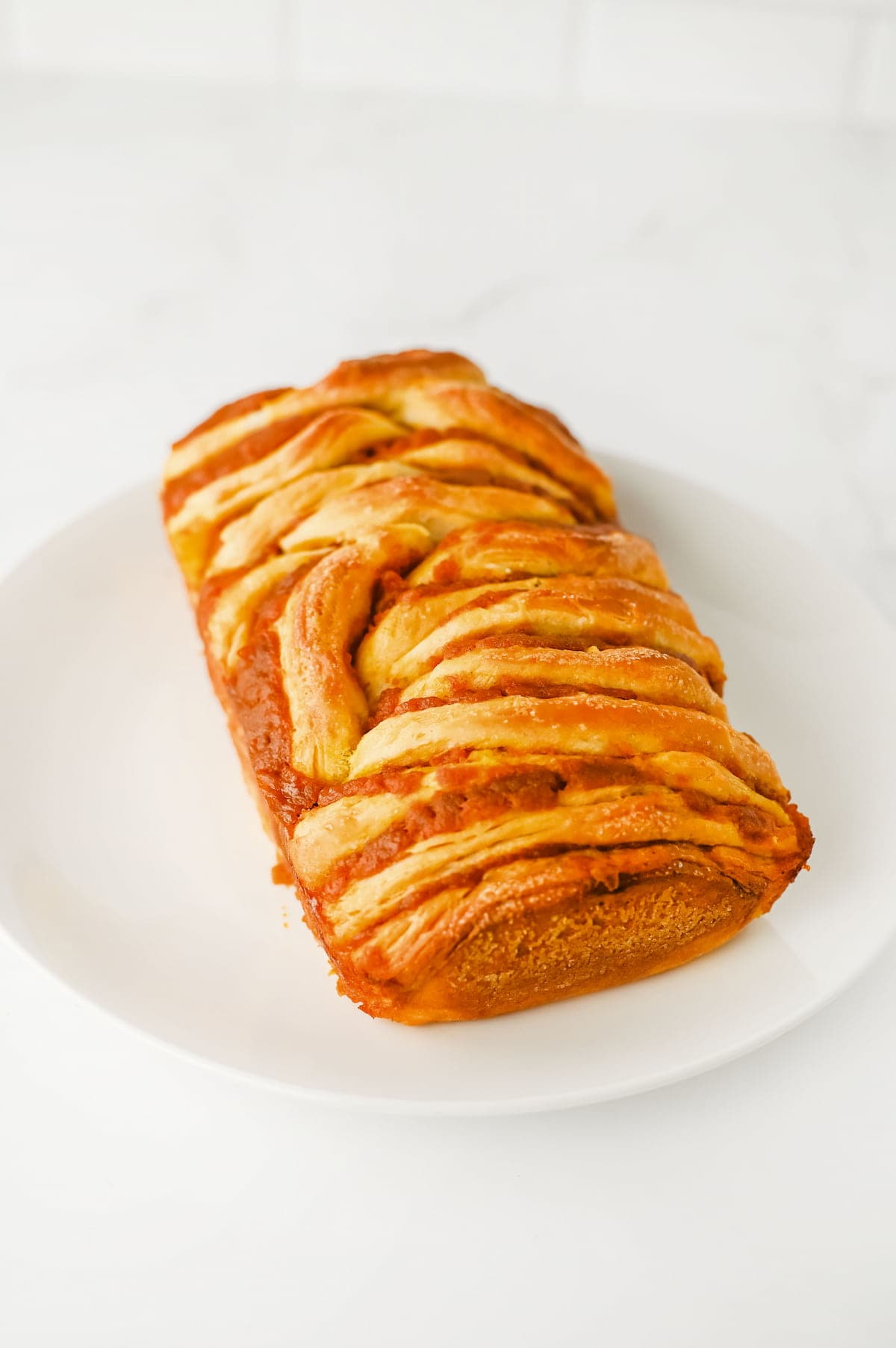 A pumpkin bread bread is displayed on a white plate against a white background.