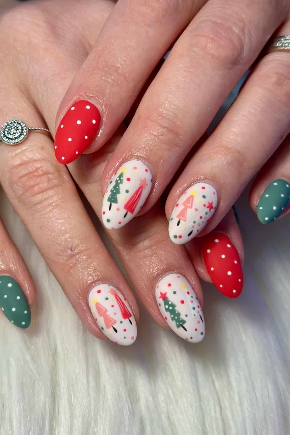 Hands with almond-shaped nails featuring festive Christmas designs, including trees, ornaments, and polka dots in red, green, and white.