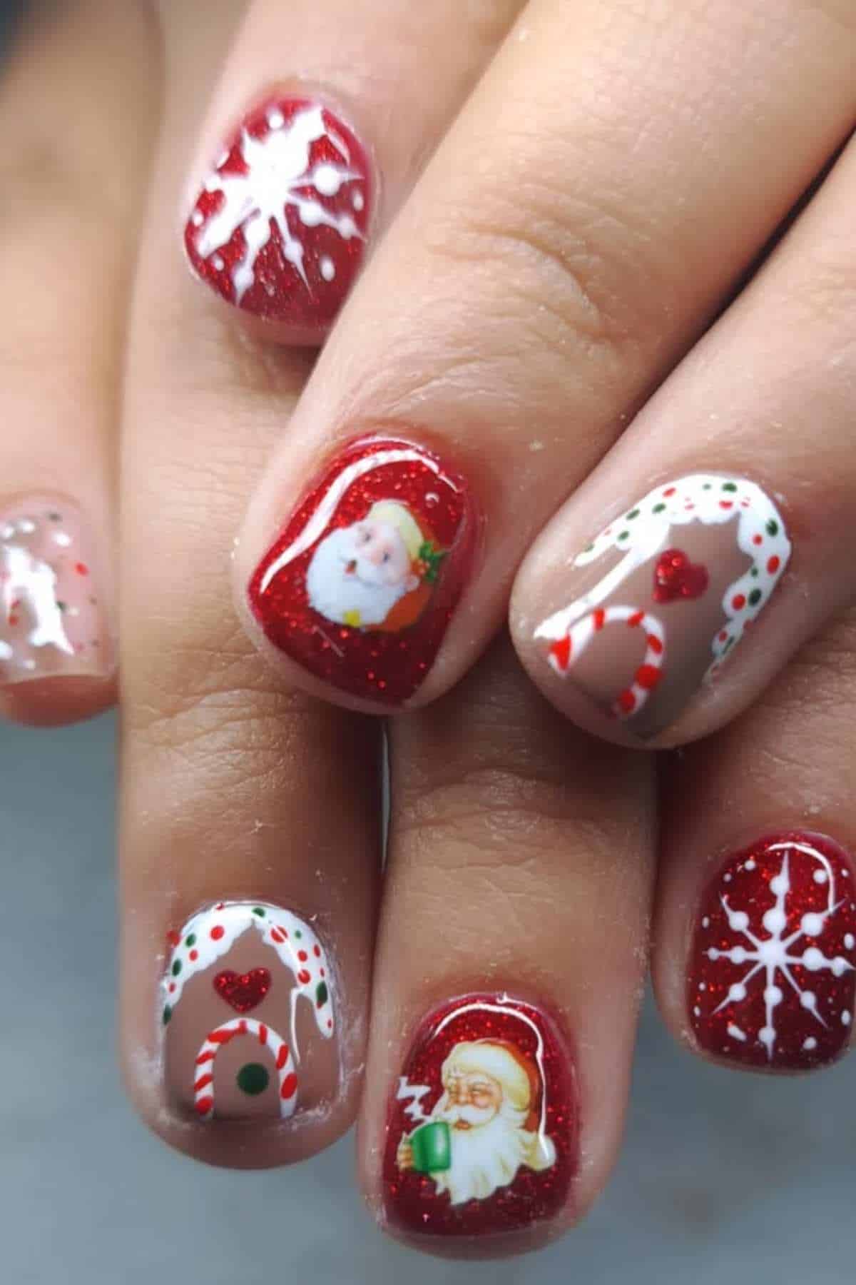 Close-up of fingernails painted with festive Christmas designs, featuring Santa Claus, candy canes, snowflakes, and gingerbread motifs on red and nude backgrounds.