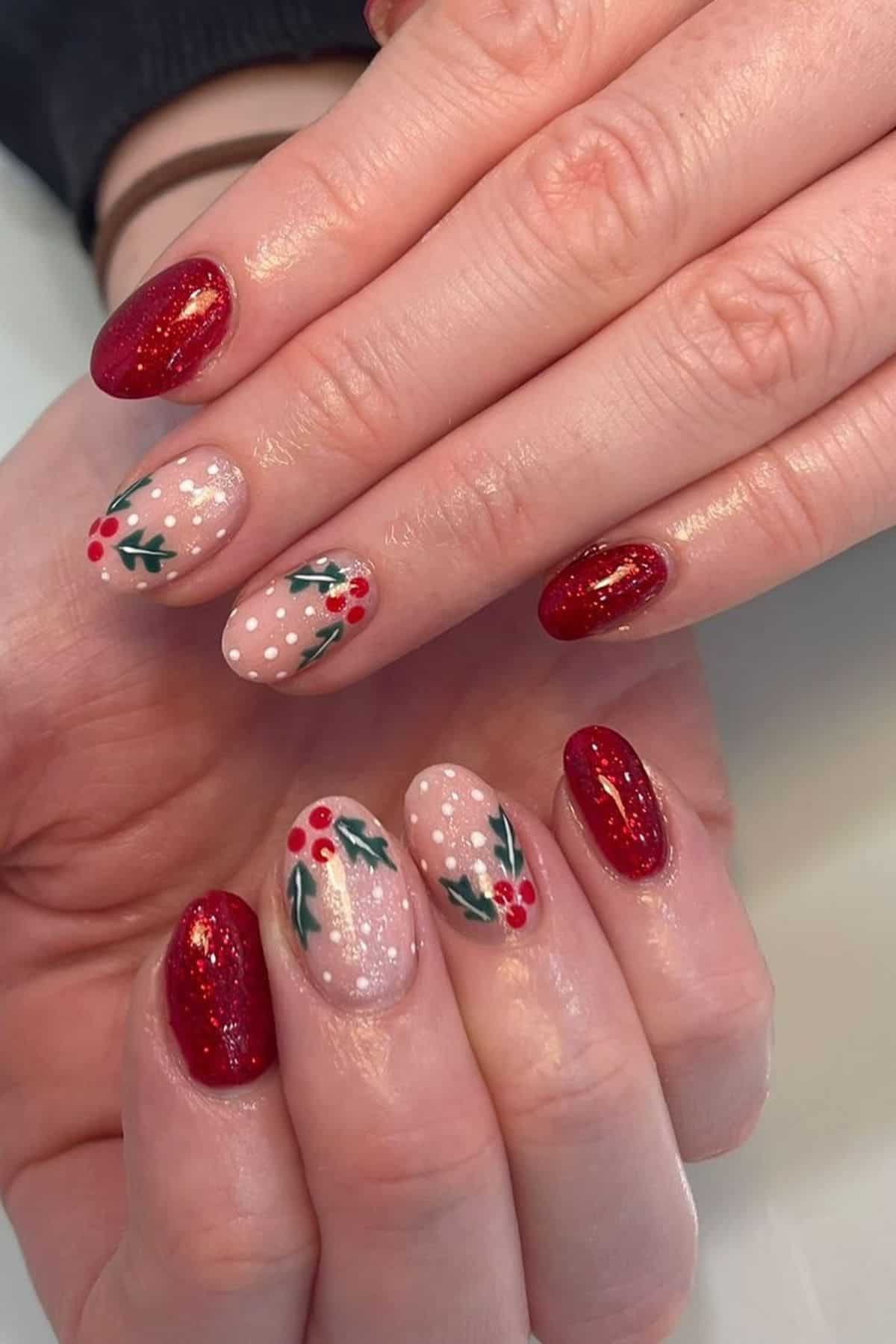 A hand with manicured nails featuring red glitter polish and nude nails decorated with white dots and holly berry designs.