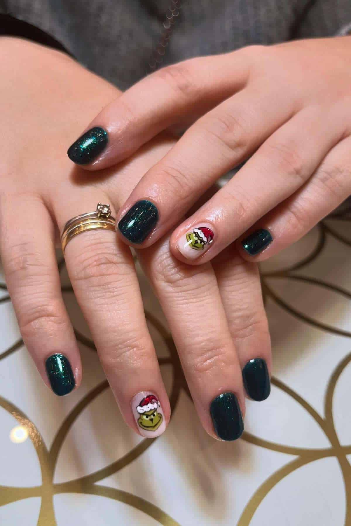Hands with dark green glittery nail polish; ring fingers feature a Grinch face with a Santa hat as nail art.