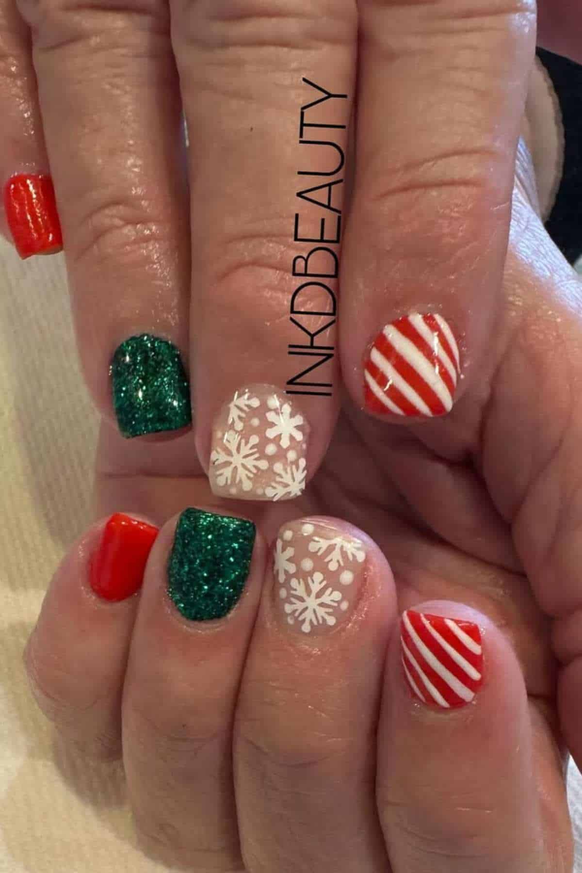 A hand with Christmas-themed nail art: red, green glitter, white with snowflakes, and red-and-white candy cane stripes.