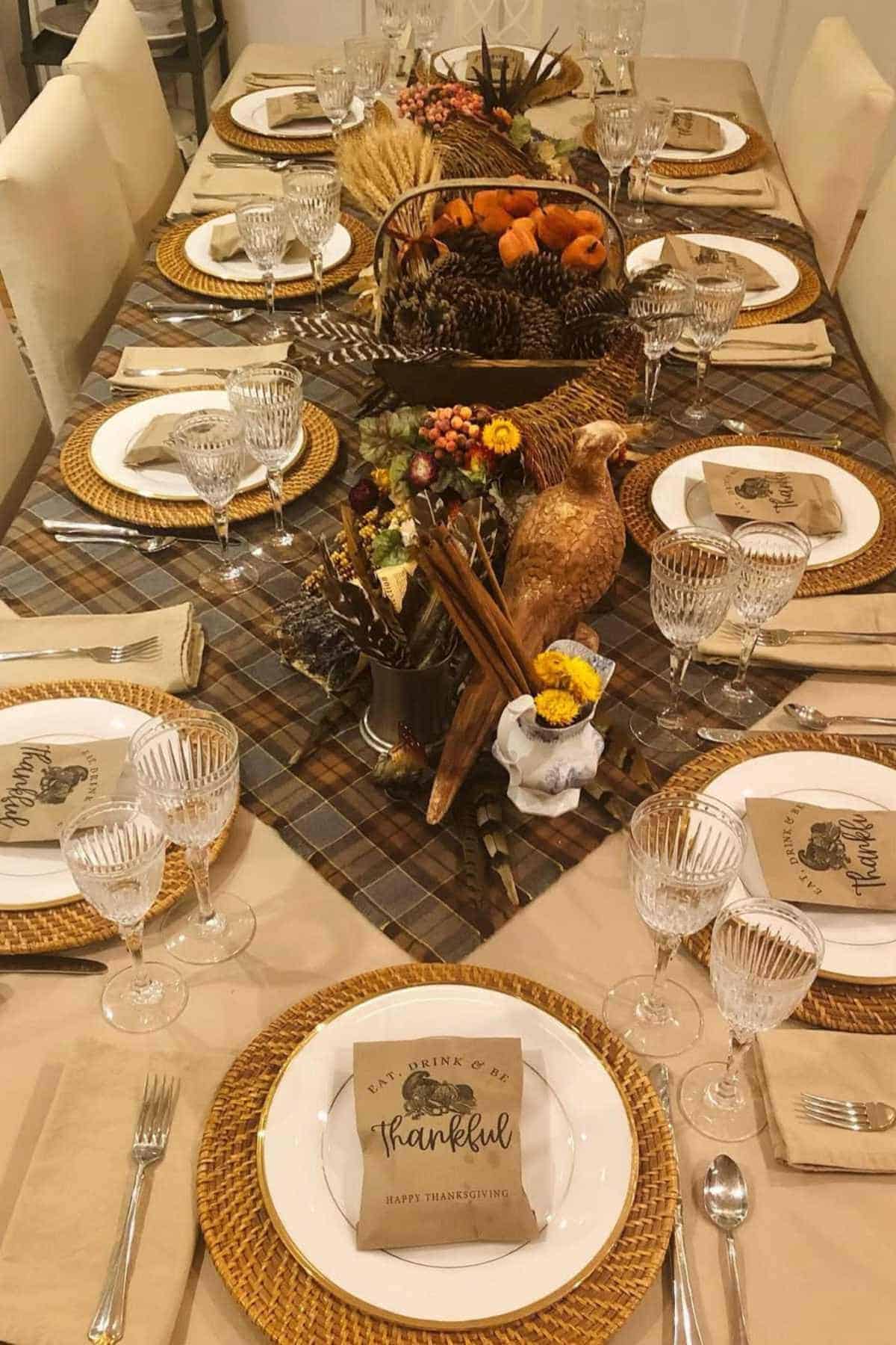 Thanksgiving table set with plates, glasses, and napkins; centerpiece features autumn decor, pinecones, and a "thankful" sign on each plate.