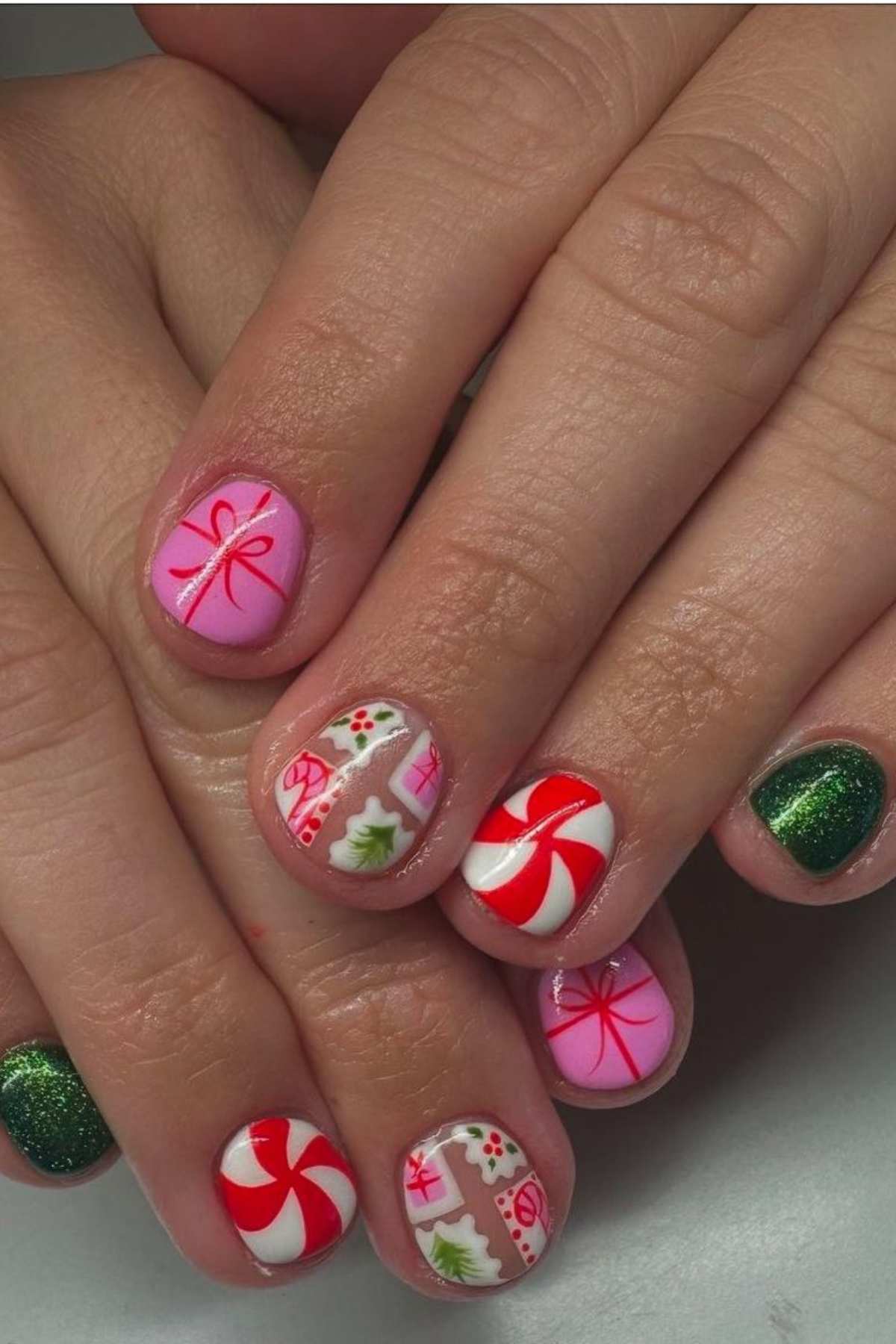 Fingernails painted with festive holiday designs, including candy canes, gift boxes, holly, red and white swirls, and green glitter polish.