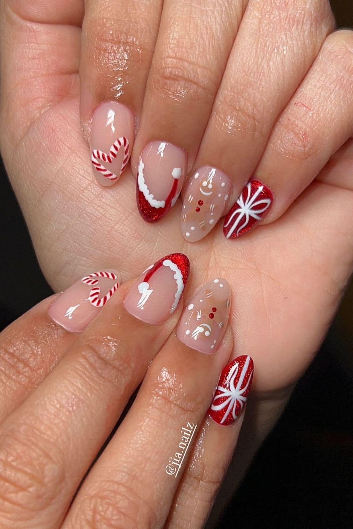 Hands with festive nail art featuring red, white, and nude colors, including candy canes, red tips, a reindeer, and a white bow design.