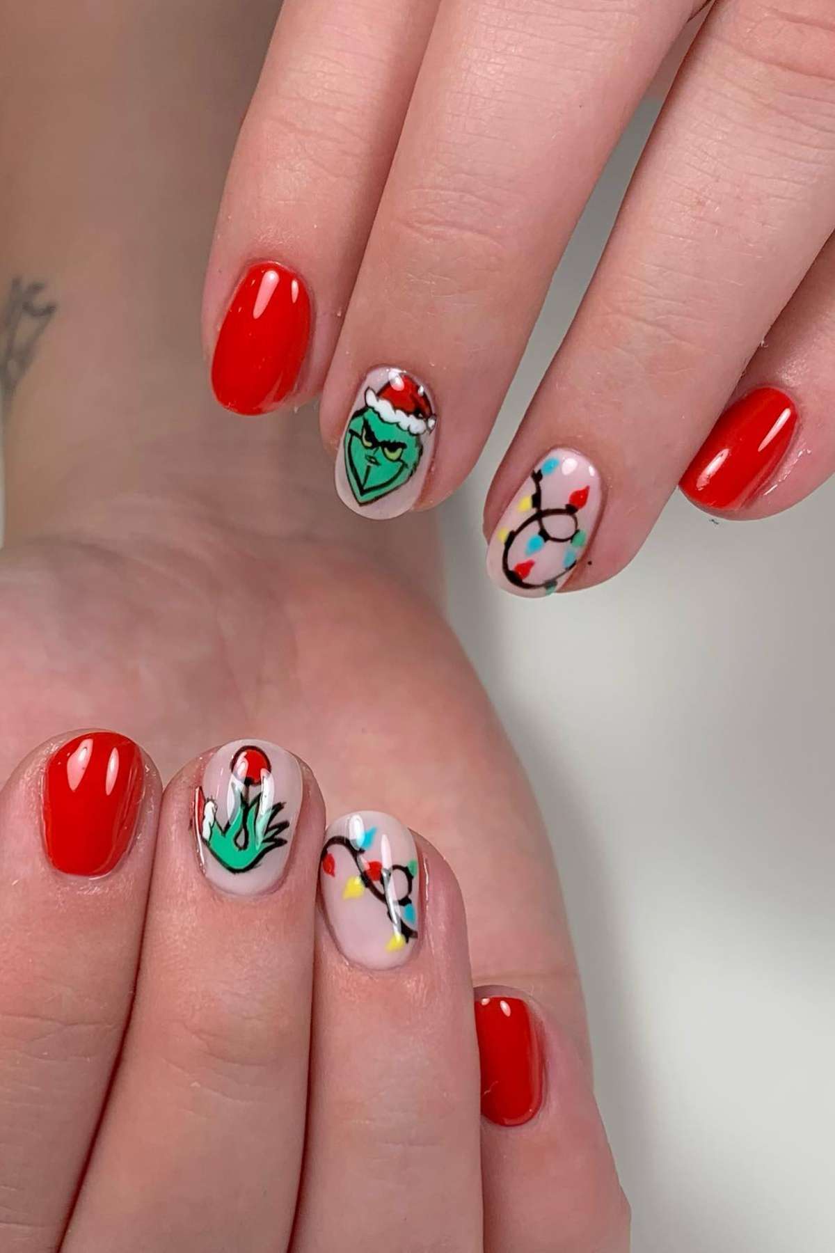 Hands with red-painted nails; some nails feature holiday-themed art including the Grinch, Christmas lights, and Santa hats.