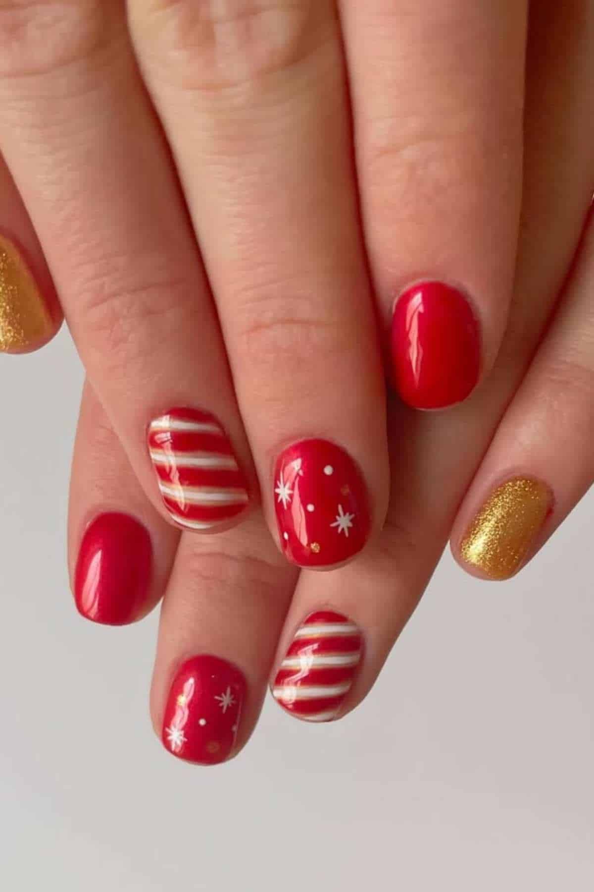 Close-up of hands with red and gold nail polish; some nails feature white star and stripe designs for a festive look.
