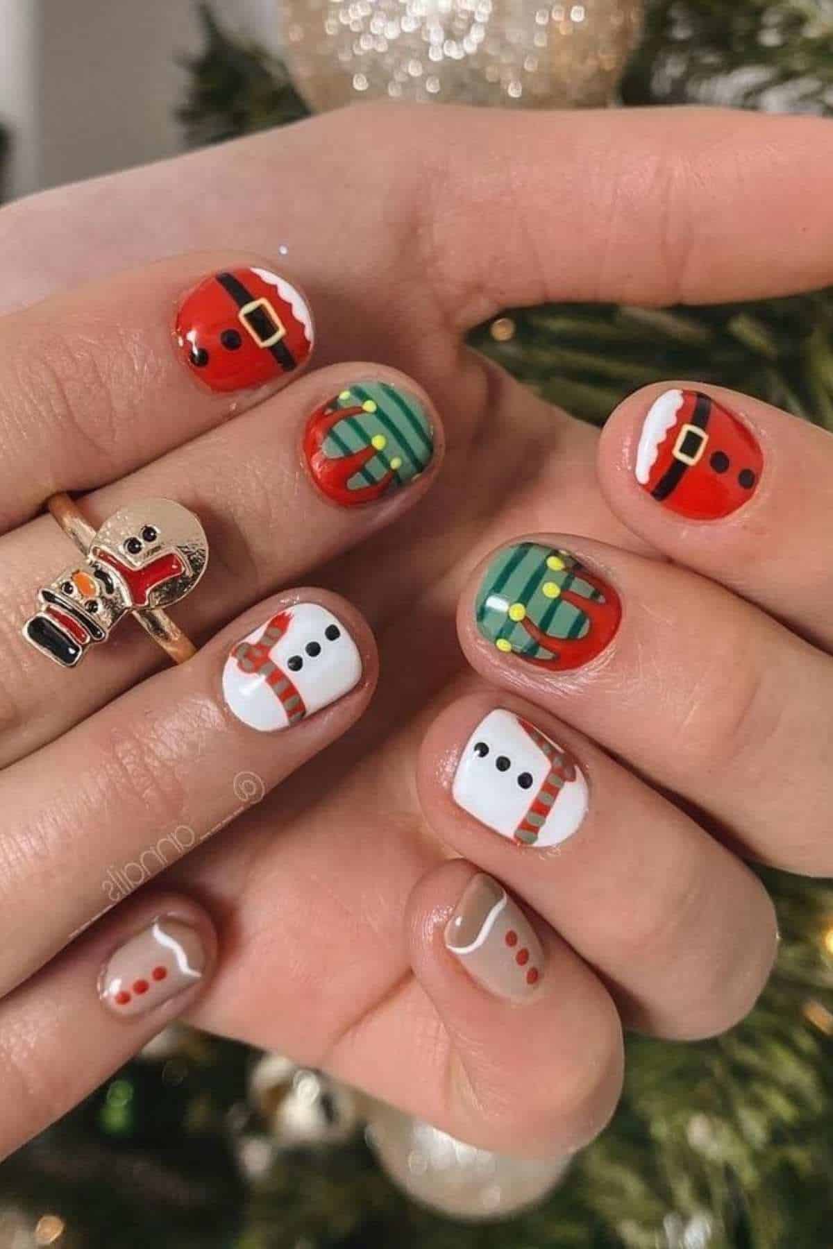 Close-up of hands with festive nail art featuring Santa suits, gift boxes, snowmen, and gingerbread designs in red, green, white, and brown tones.