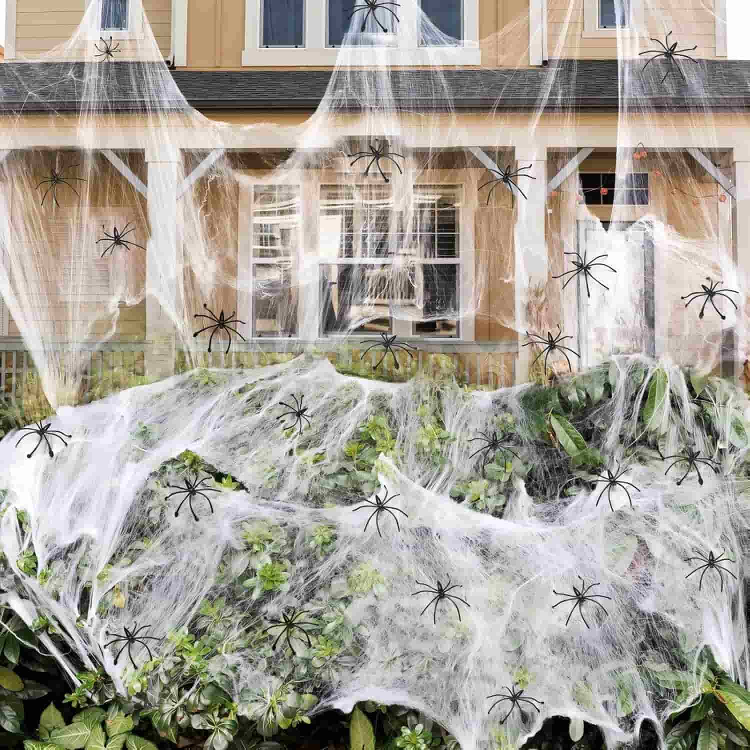 A house front decorated with fake spider webs and numerous plastic spiders spread across bushes and a porch for Halloween.