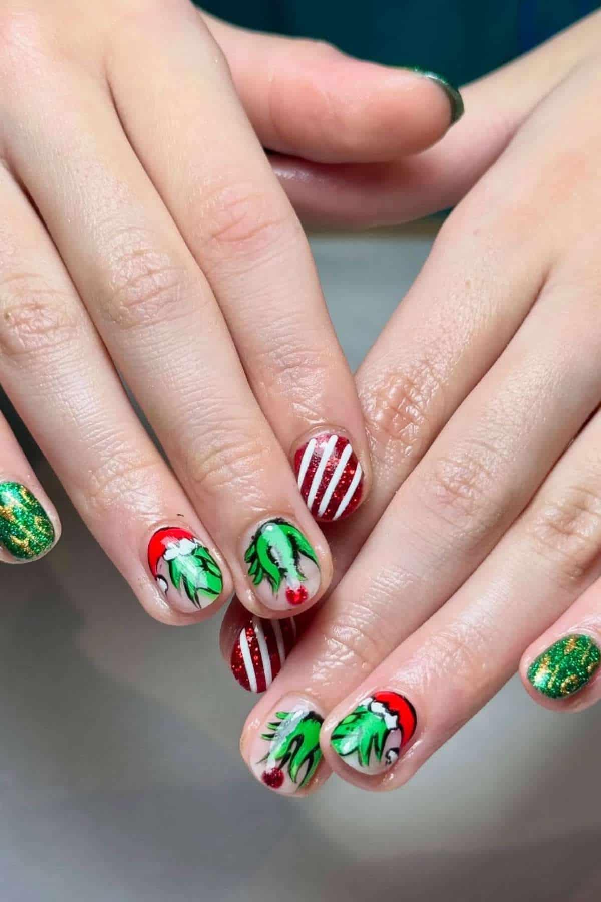 Hands with festive Christmas-themed nail art featuring holly leaves, red and white stripes, gold glitter, and Santa hat designs.