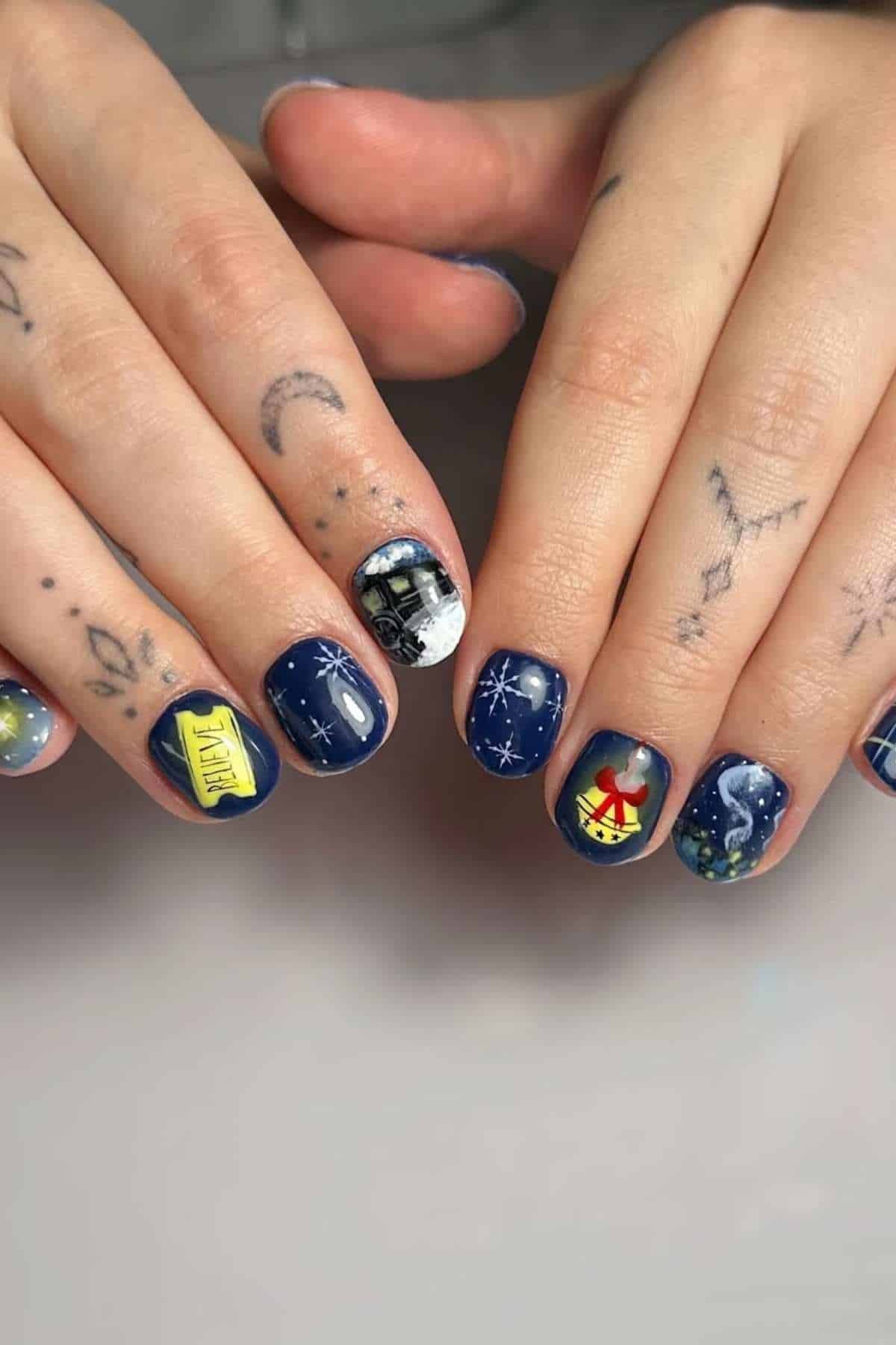 Close-up of hands with navy blue space-themed nail art featuring stars, a rocket, planets, and a yellow taxi design; small hand tattoos are also visible.