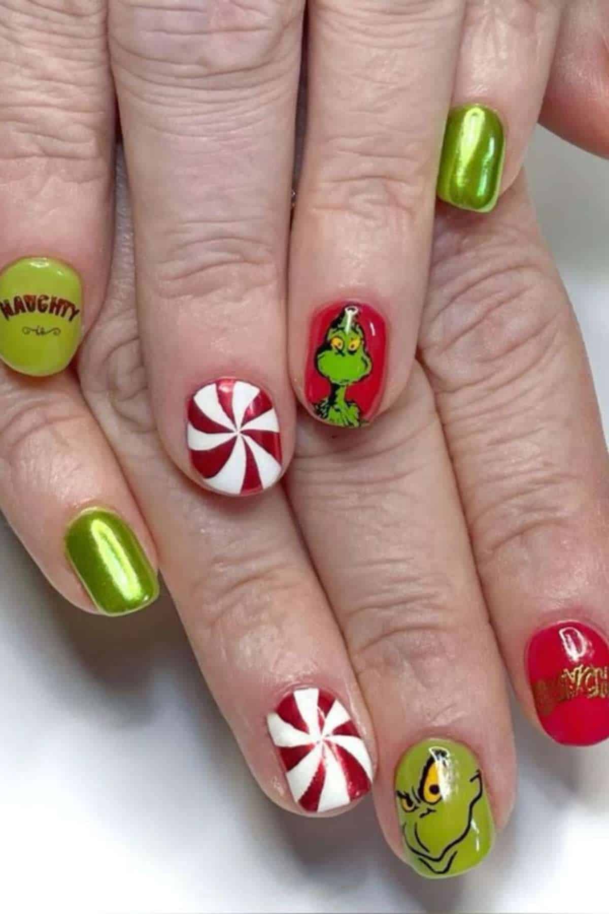 Hands with Christmas-themed nail art featuring green, red, and white nails, Grinch faces, candy swirl designs, and the word "Naughty" on one nail.