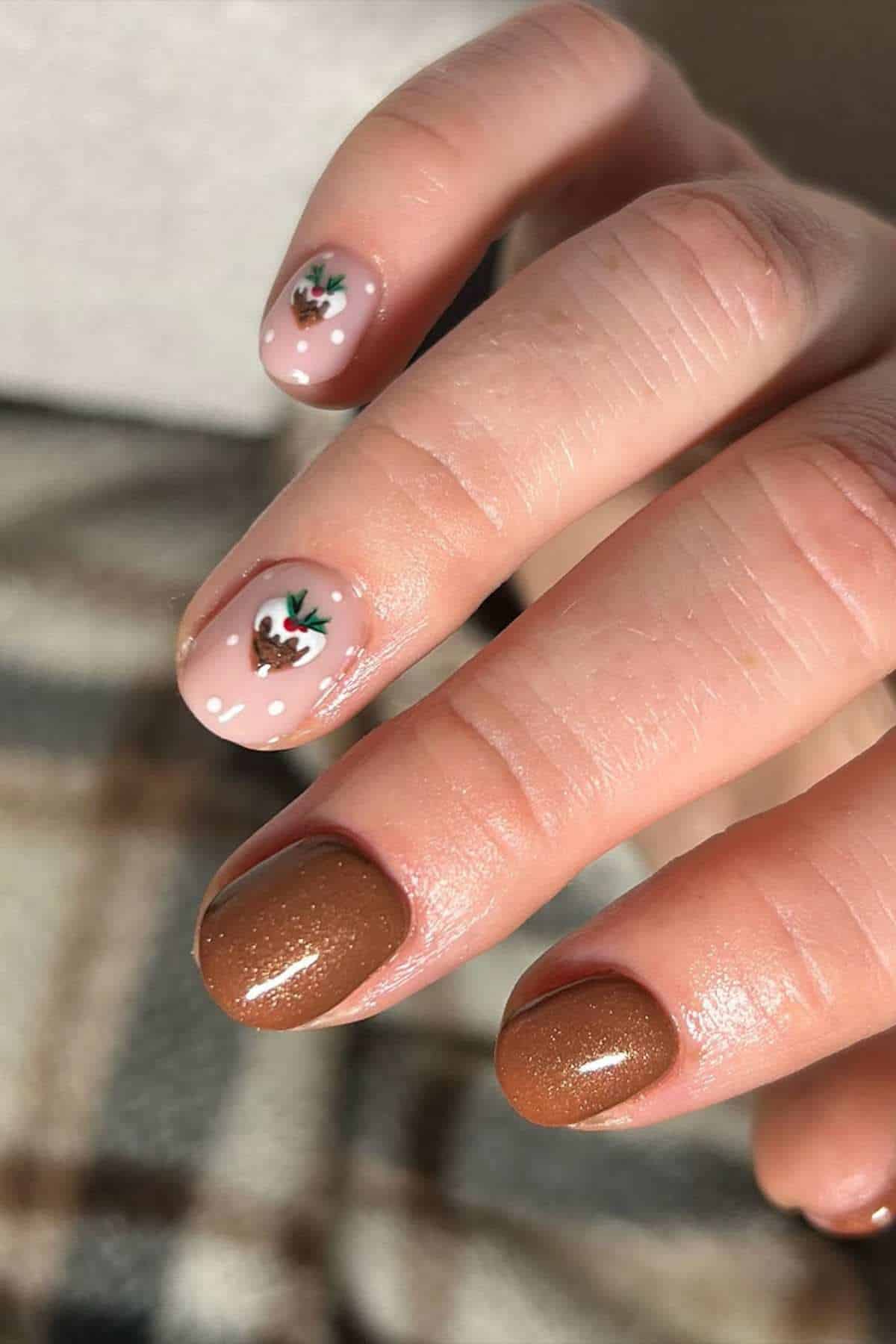 A hand with manicured nails; two nails are painted brown with shimmer, and two are light pink with small leaf designs near the cuticles.