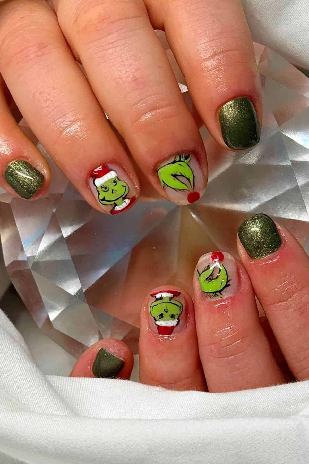 Close-up of hands with green shimmery nails; some nails feature painted designs of the Grinch’s face and Santa hat.