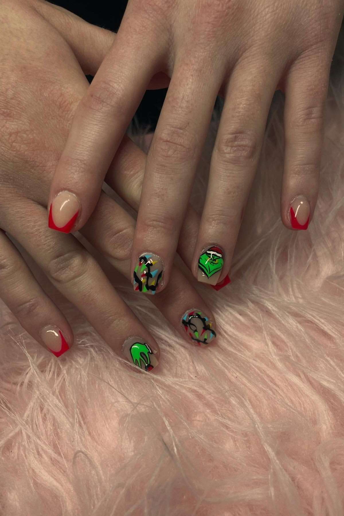 Hands with red French tip nails; ring and middle fingernails feature colorful abstract designs and green faces. The hands rest on pink faux fur.