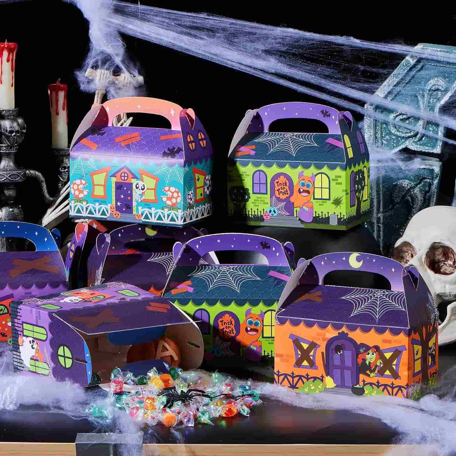 Halloween-themed treat boxes decorated with haunted houses and cartoon characters, displayed on a table with scattered candy, skulls, candles, and cobwebs in the background.