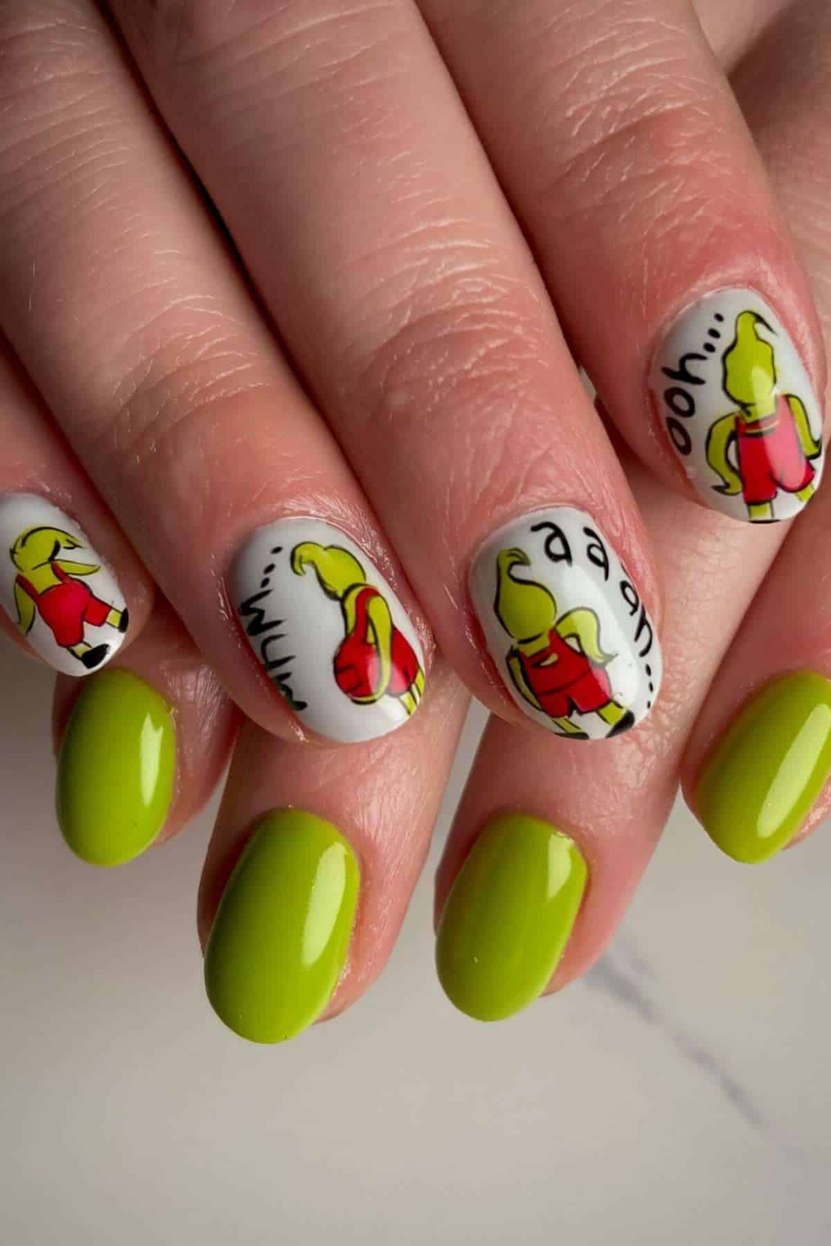 A close-up of hands with manicured nails; some nails are painted lime green, while others feature cartoonish yellow-green figures on a white background with black text.