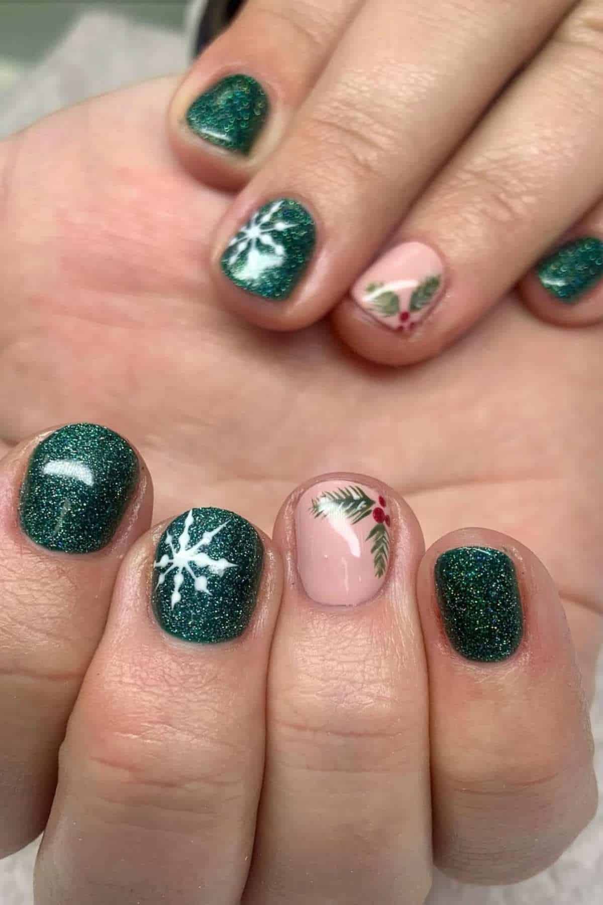 A hand with green glittery nails, featuring a white snowflake design on one nail and a pink nail with holly and pine branch accents.
