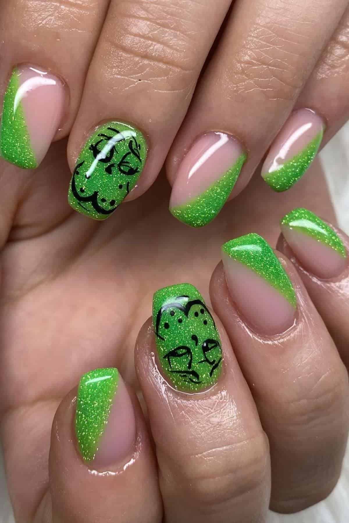 Hands with green glitter French tip nails; two nails feature black outlined abstract animal faces on the green tips.