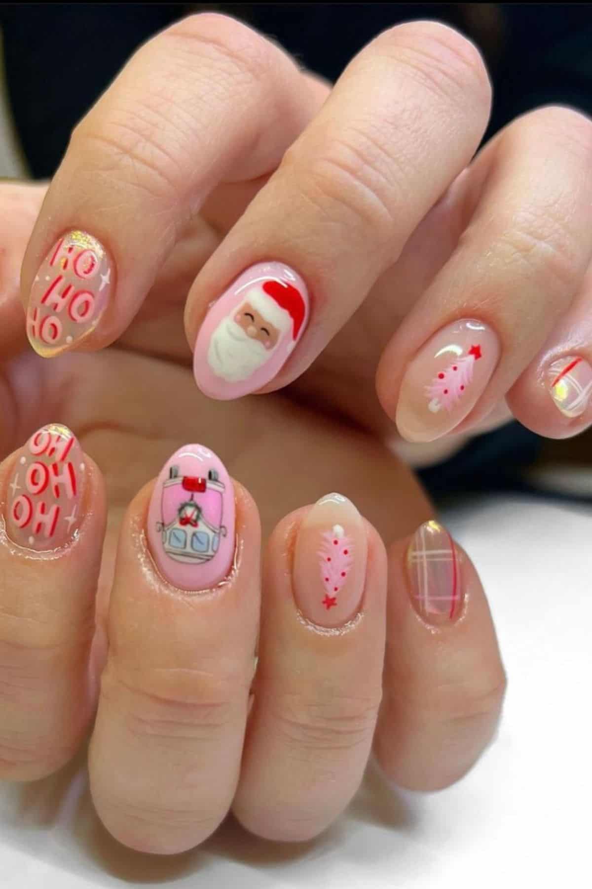 A hand with festive nail art featuring a Santa face, Christmas trees, “HO HO HO” text, a present, and red-and-pink plaid designs on each fingernail.