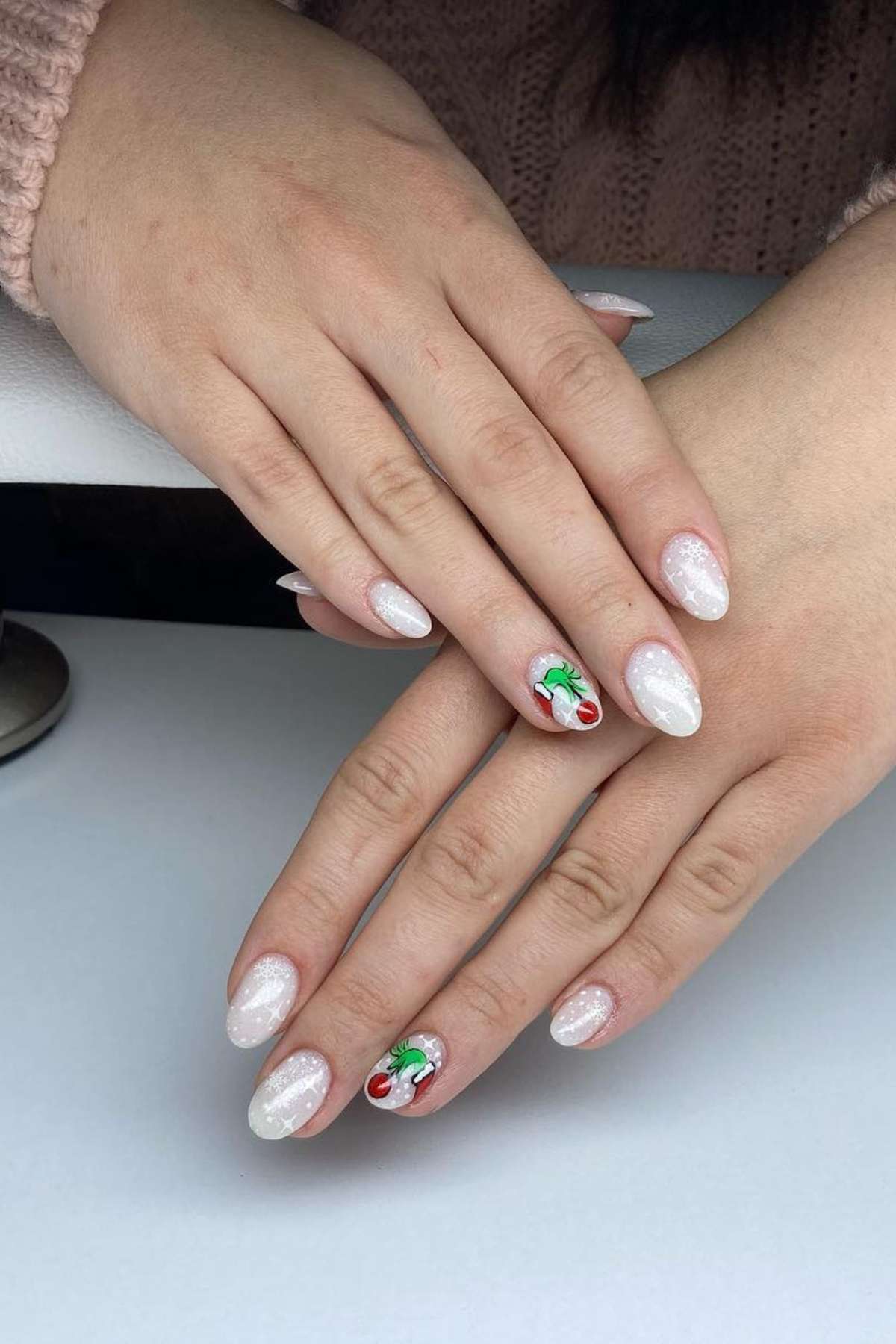 Hands with almond-shaped, glittery white nails; ring fingers feature the grinch's finger.