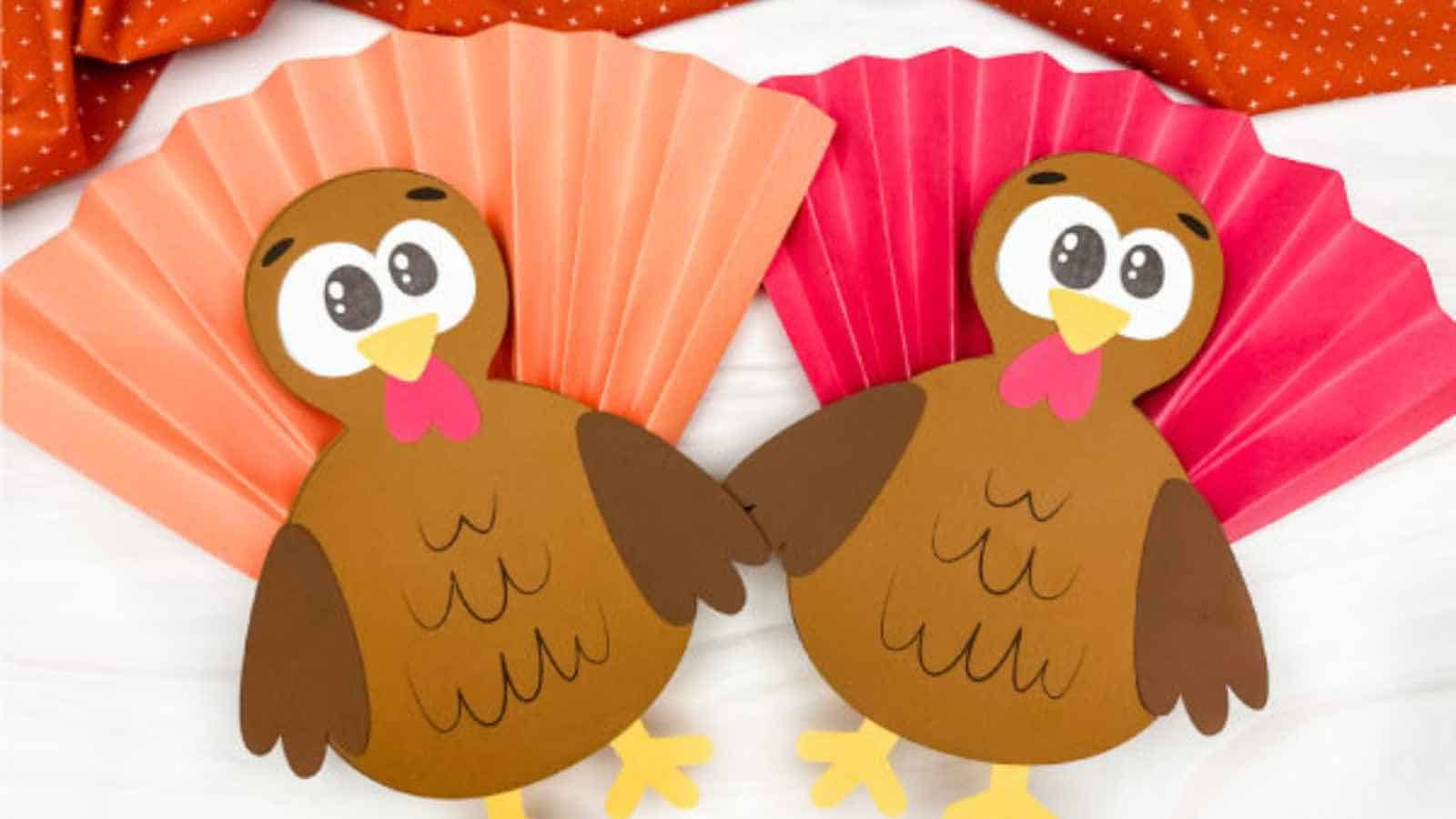 Two paper turkeys made from brown, orange, and red craft paper with fan-shaped tails, placed on a white surface.