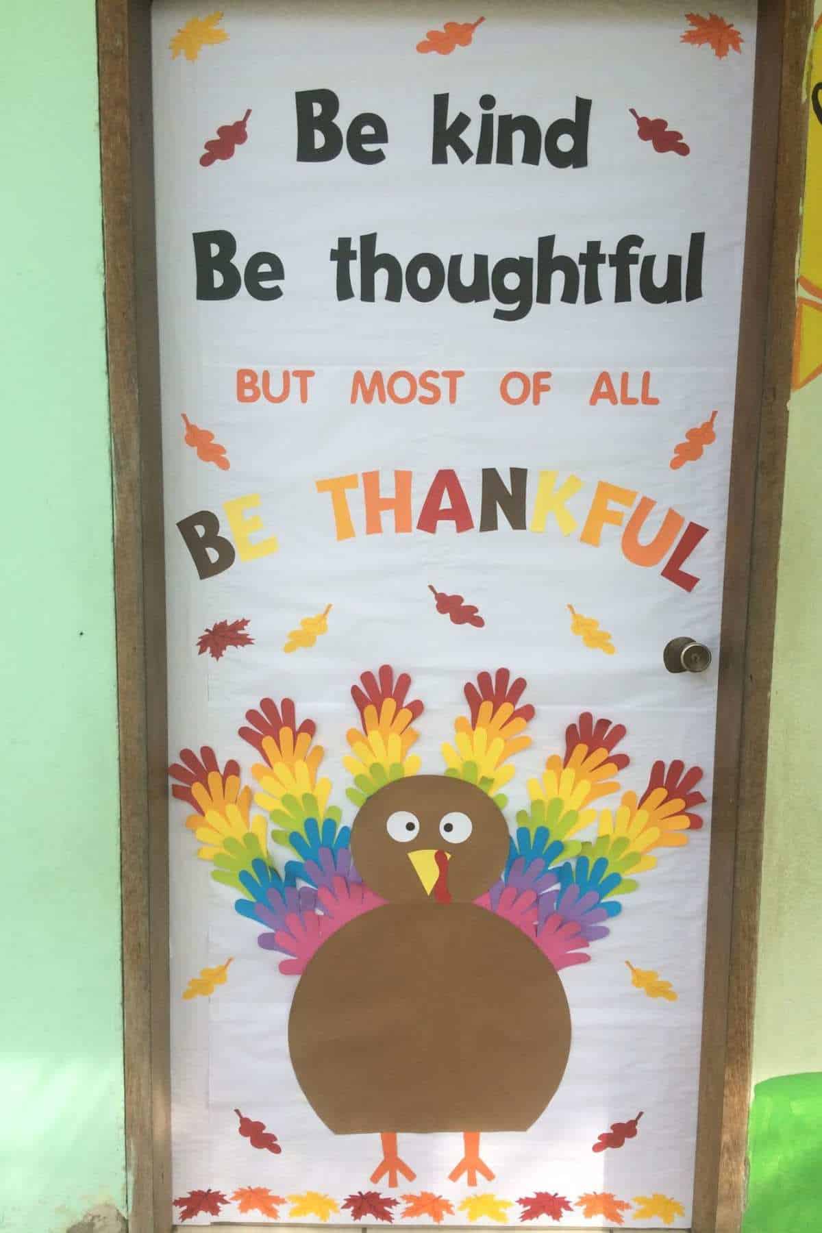 A door decorated with a large paper turkey and colorful feathers, along with the text: "Be kind, Be thoughtful, but most of all Be thankful," and paper leaves.