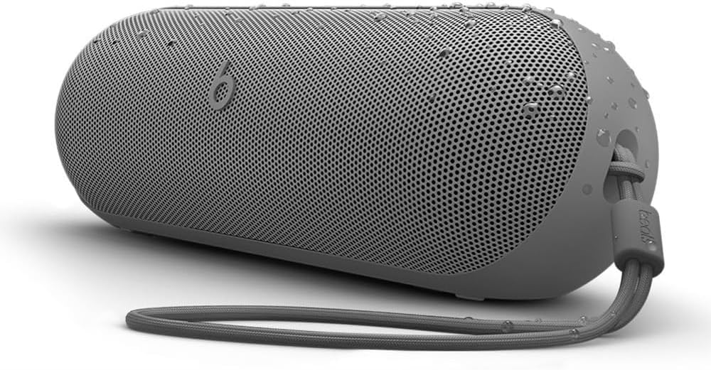 A gray portable Bluetooth speaker with a wrist strap, shown with water droplets on its surface, indicating water resistance.