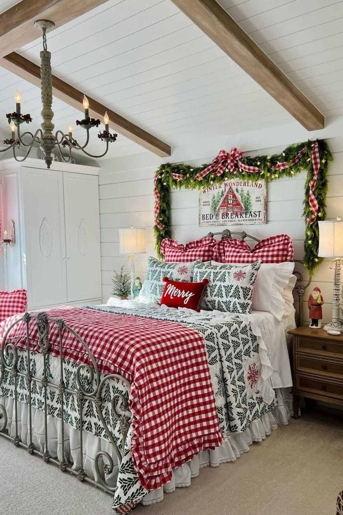 A cozy bedroom decorated for Christmas with red and green bedding, a "Merry" pillow, garlands, Christmas signs above the bed, and festive ornaments on the nightstands.