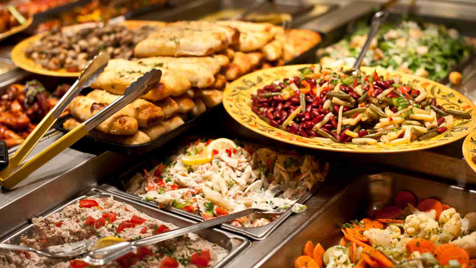 A buffet table with trays of assorted dishes, including breadsticks, salads, mixed vegetables, and various cooked entrees.