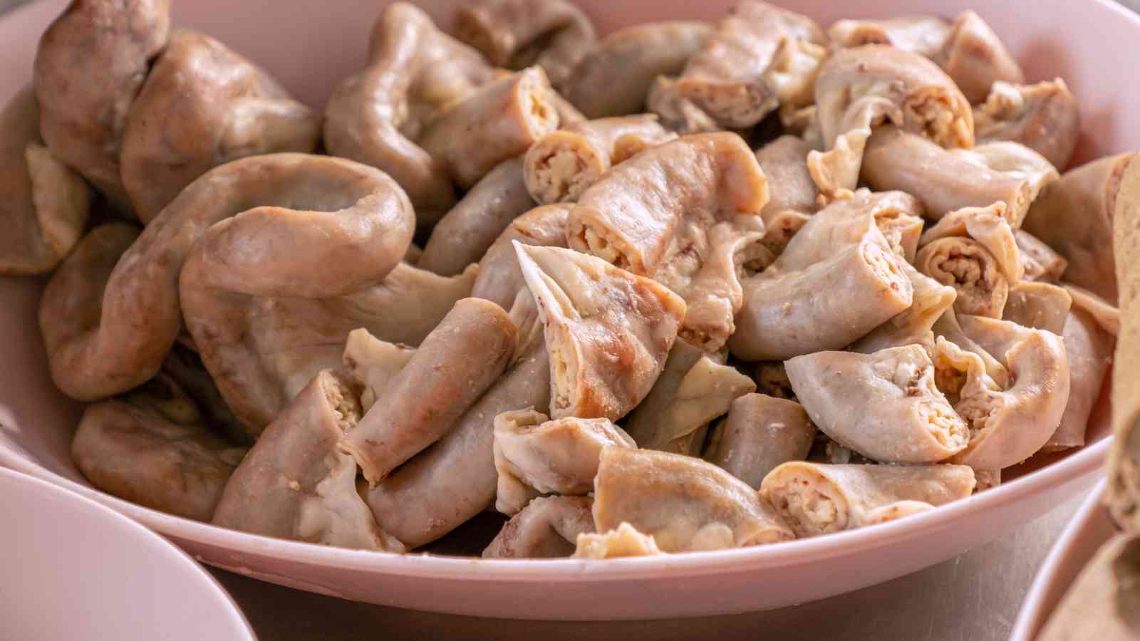 A bowl filled with pieces of cooked pork intestines, cut into sections and arranged closely together.