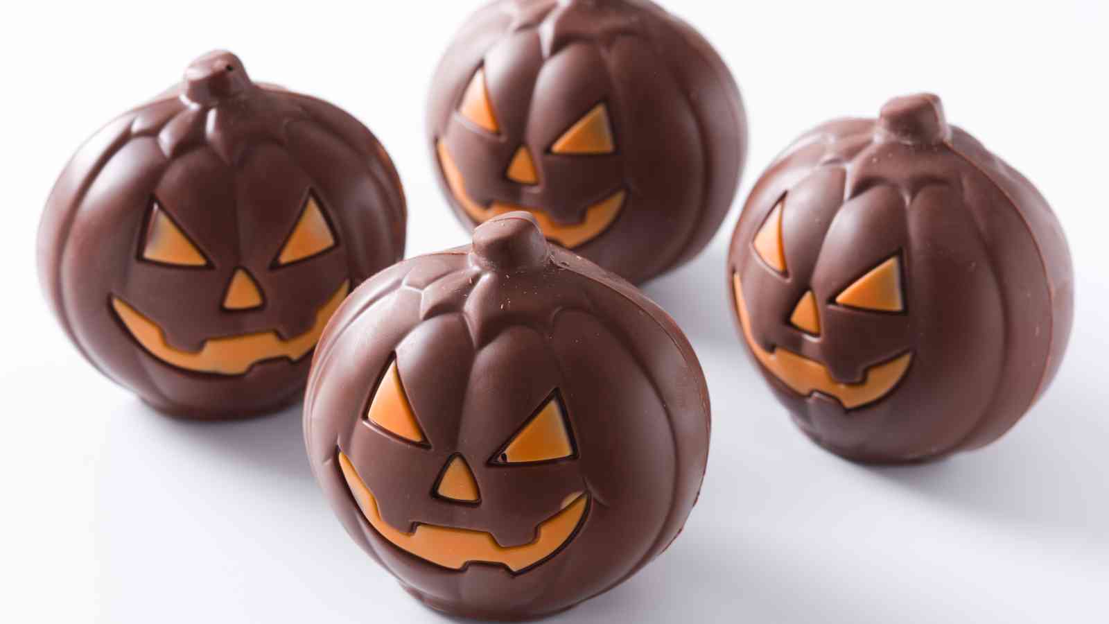 Four chocolate candies shaped like jack-o'-lantern pumpkins with orange facial features, arranged on a white background.