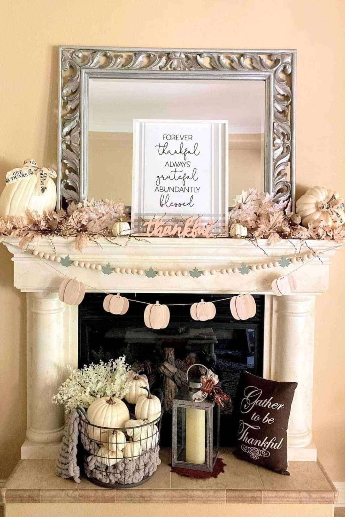 A decorated fireplace mantel with pumpkins, flowers, a mirror, a sign reading “Forever thankful, always grateful, abundantly blessed,” and autumn-themed garlands and pillows.
