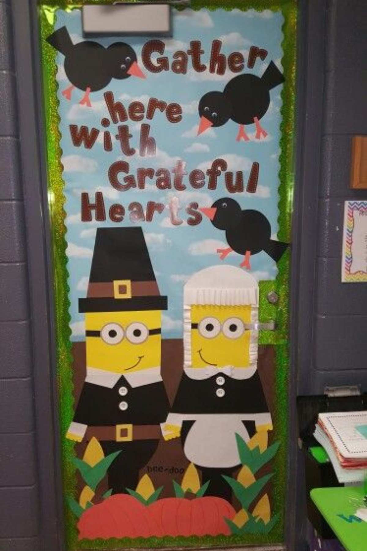 A classroom door decorated with Minions dressed as pilgrims, black birds, and the text "Gather here with Grateful Hearts" in large letters.
