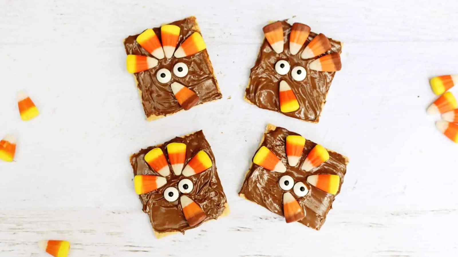 Four square chocolate treats decorated with candy corn and candy eyes to resemble turkeys, arranged on a white surface.