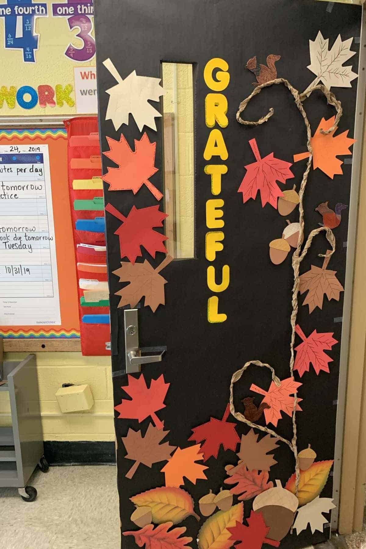 A classroom door decorated with colorful autumn leaves, acorns, and vines, featuring the word "GRATEFUL" spelled vertically in yellow letters.