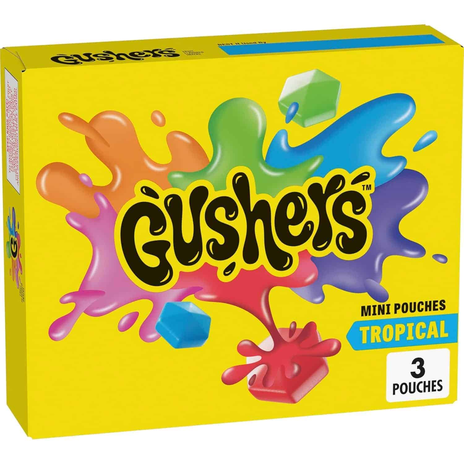 A yellow box of Gushers Tropical Mini Pouches with colorful splashes and fruit-shaped gummies on the front. The box contains 3 pouches.