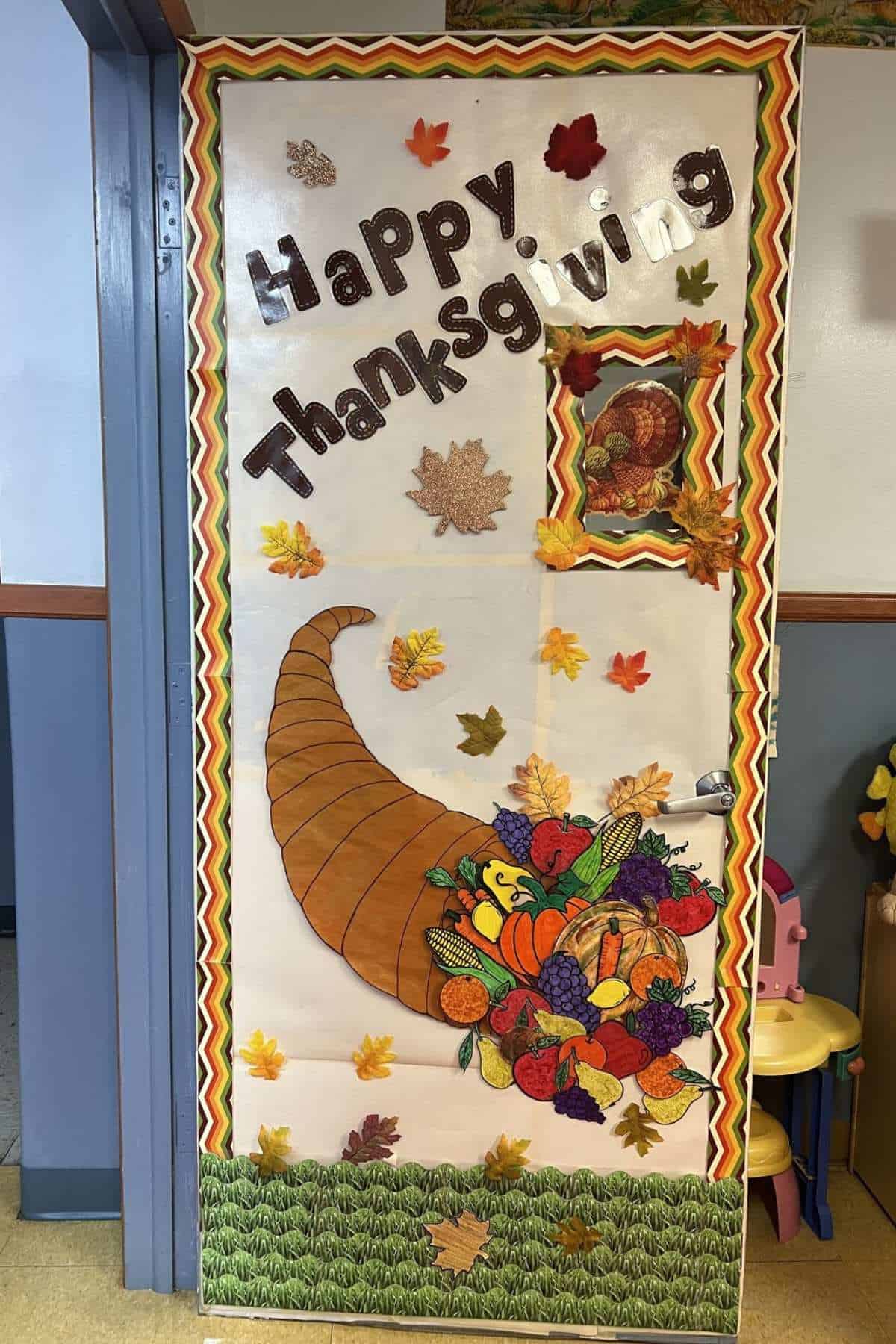 A classroom door decorated with a "Happy Thanksgiving" sign, a cornucopia with fruits and vegetables, fall leaves, and a turkey image.