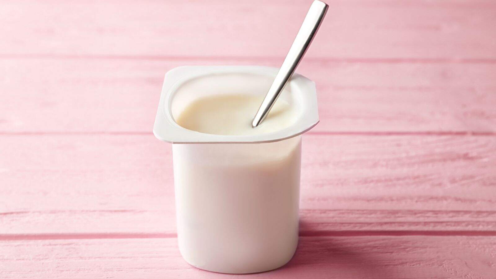 Yogurt container with spoon on pink wooden background, healthy parenting snack, thriving in parenting SEO image.