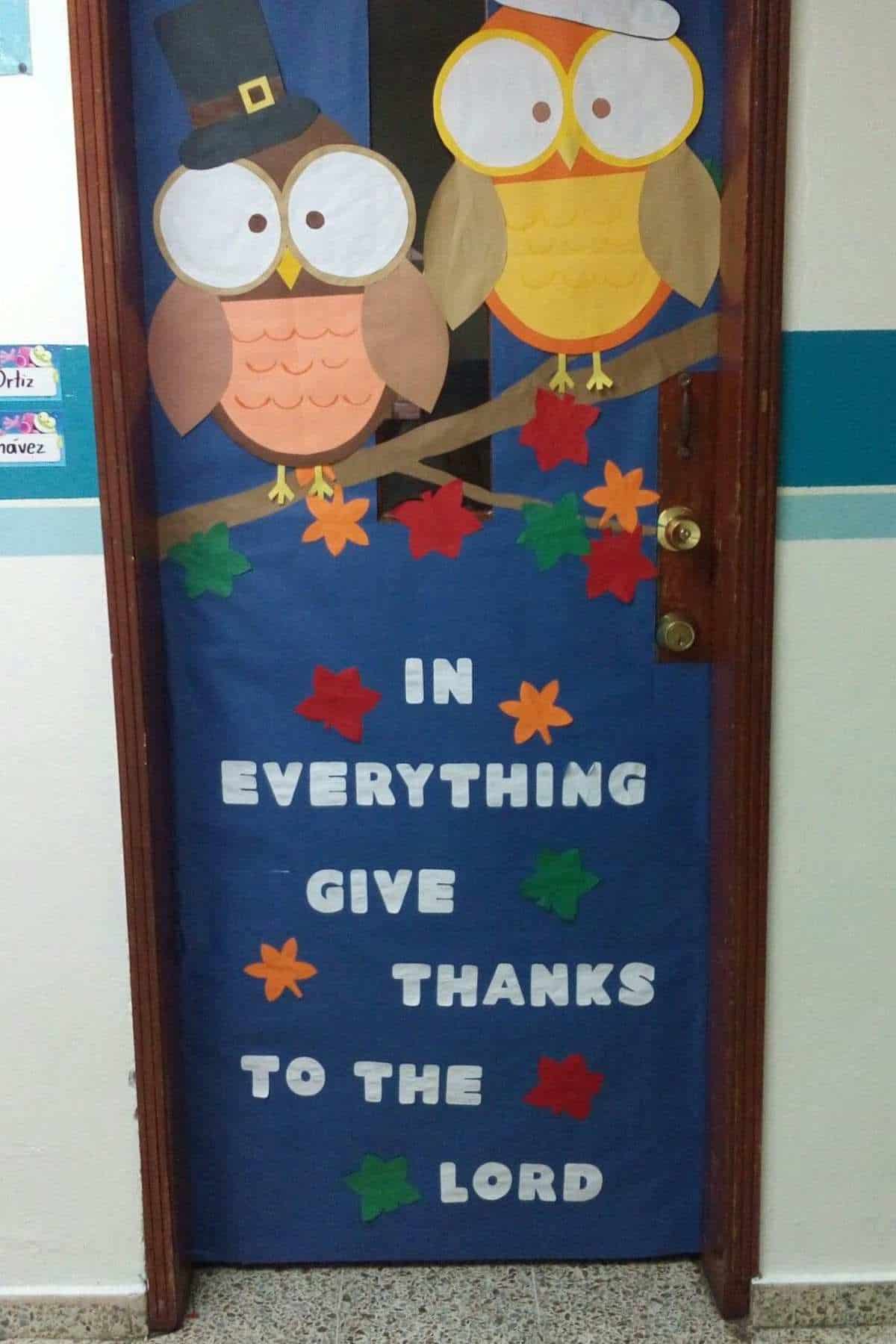 A door decorated with two paper owls, colorful leaves, and the words “In everything give thanks to the Lord.”.