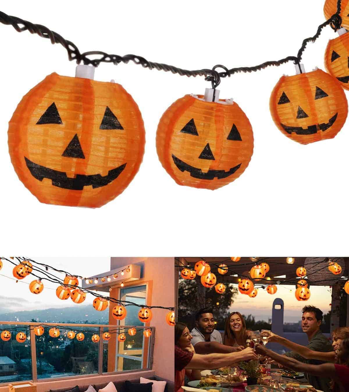 String lights with orange pumpkin lanterns are hung outdoors, including above a group of people gathered around a table at a patio party.