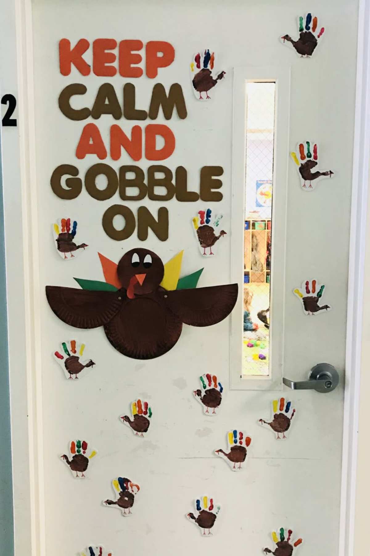 A white door decorated with paper turkeys and the phrase “KEEP CALM AND GOBBLE ON” in large letters, featuring a large turkey made from a brown paper plate.